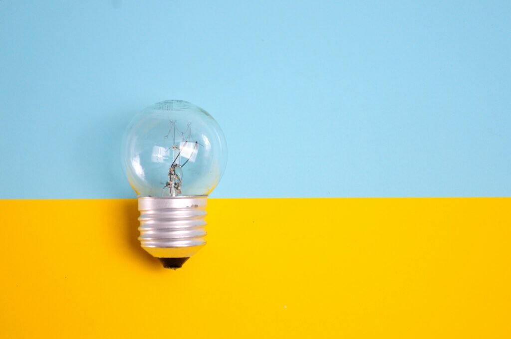 A clear light bulb against a vibrant blue and yellow background, symbolizing energy and creativity.